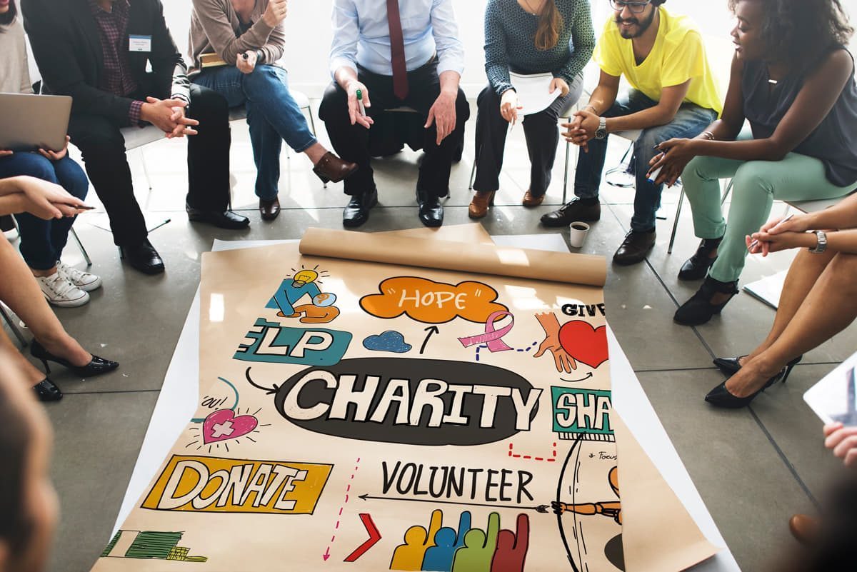 Eine Gruppe von Menschen sitzt um ein Blatt Papier herum, auf dem das Wort „Wohltätigkeit“ steht, und demonstriert ihr Verbraucherverhalten und ihre soziale Verantwortung durch eine Marketinginitiative.